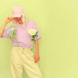 Laughing woman wearing cap with flowers standing against colored background