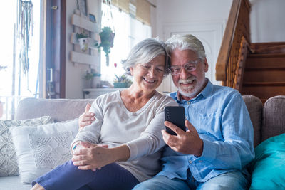 Senior couple looking at mobile phone while sitting on sofa at home