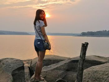 Woman standing on rock against sky during sunset