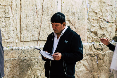 Young man using mobile phone while standing against wall