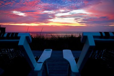 Empty seats by sea against sky during sunset