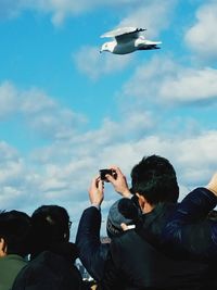 Low angle view of friends photographing against sky