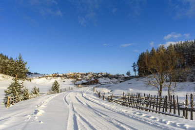 Snow covered road by trees against sky