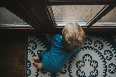 High angle view of baby boy looking through wet window at home