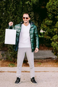 Portrait of man wearing sunglasses holding bag standing outdoors