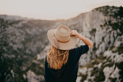 Rear view of woman wearing hat looking at mountains during sunset