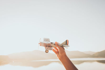 Low angle view of hand holding toy airplane against clear sky