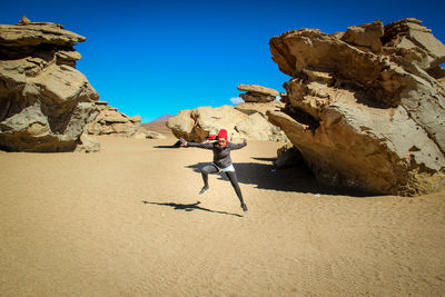 Woman on rock formations against clear blue sky