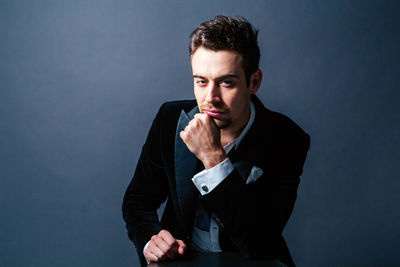 Portrait of young man sitting against gray background