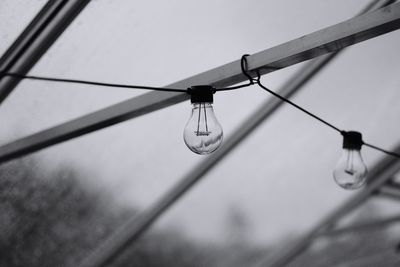 Low angle view of light bulbs hanging on metal rod against sky