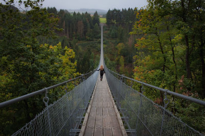 Woman on footbridge amidst trees in forest