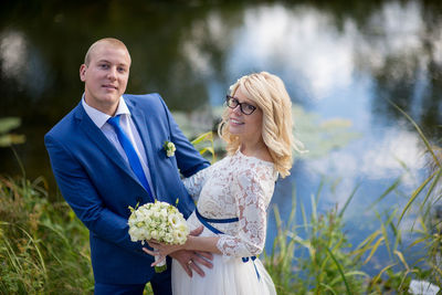 Portrait of newlywed couple standing by pond
