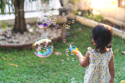 Little asian girl playing with soap bubbles in garden.