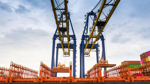 Low angle view of crane and cargo container against cloudy sky