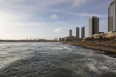 Sea by city buildings against sky