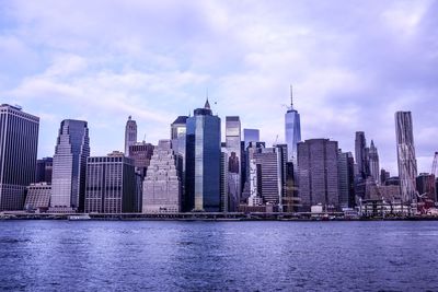 Modern buildings by river against sky in city