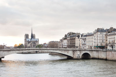 Bridge over river in city against cloudy sky