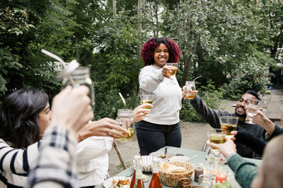 Young woman toasting drinks with multiracial friends during dinner party in back yard