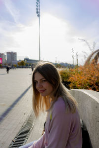 Portrait of smiling young woman in city against sky