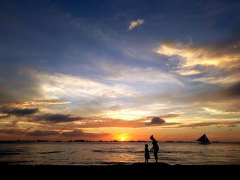 Silhouette people on beach against sky during sunset