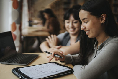 Smiling female students discussing over book at library