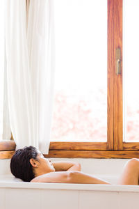 Rear view of woman relaxing on bed at home