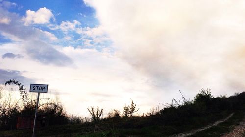 Road passing through field against cloudy sky