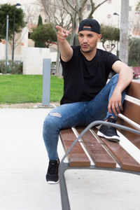 Young man pointing while sitting on bench at park