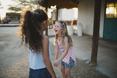 Girl laughing while standing with sister at farm during sunset