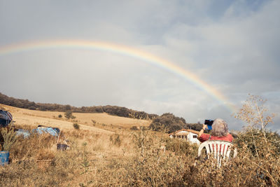 Rear view of people sitting on field against rainbow in sky