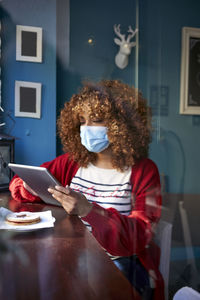 Woman wearing sanitary mask using digital tablet while sitting at home