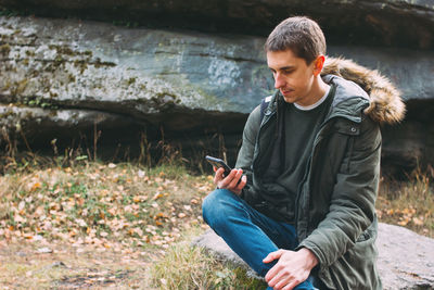 Man holding mobile phone while sitting on land