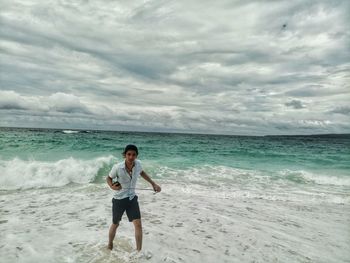 Portrait of man holding monopod while walking on shore at beach against cloudy sky