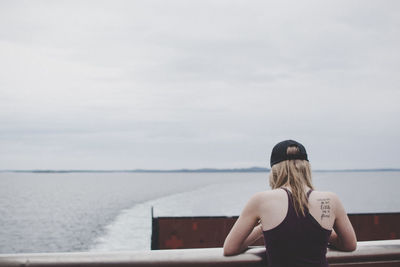 Rear view of woman sitting on sea shore against sky