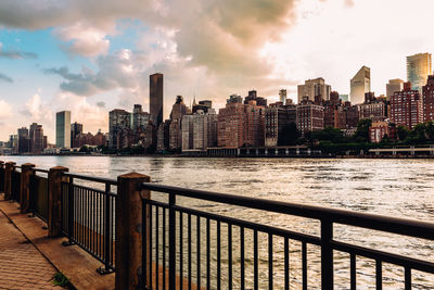 Modern buildings by river against sky in city