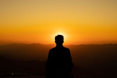 Silhouette man looking at mountain against orange sky