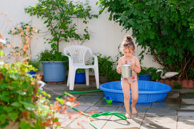 Cute young girl watering plants with a bucket on a summer day in the backyard