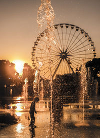 Illuminated ferris wheel against sky during sunset