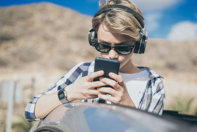 Boy wearing sunglasses listening to music while using phone in car