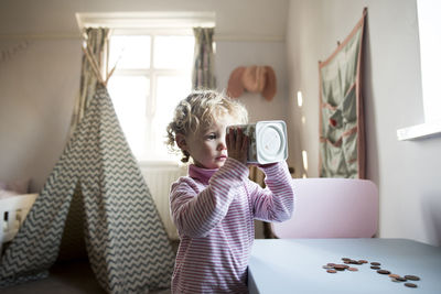 Girl looking in piggy bank while standing by table at home