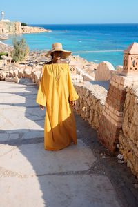 Happy african american woman in yellow dress and sun hat enjoys view of coast of red sea on natural 