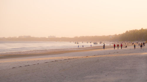 Group of people on beach against clear sky during sunset