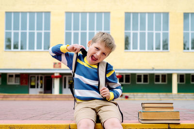 Portrait of smiling boy sitting against school building