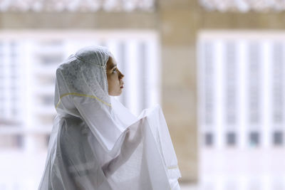 Side view of young woman wearing hijab while praying in mosque