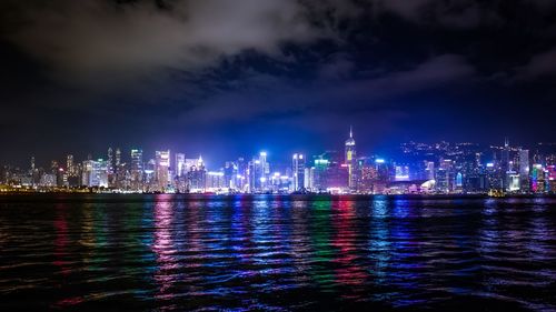 Illuminated city and river against sky at dusk