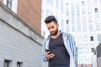Young man using mobile phone while standing against buildings