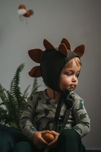 Toddler baby boy in funny dino costume sitting with eggs in hands