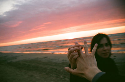 Woman holding man hand at beach against cloudy sky during sunset