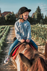 Little smiling girl learning horseback riding. 5-6 years old equestrian in helmet