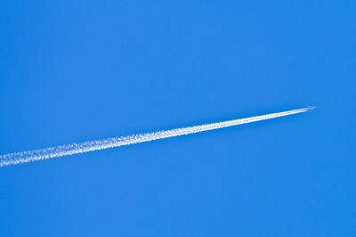 Low angle view of vapor trails against clear blue sky